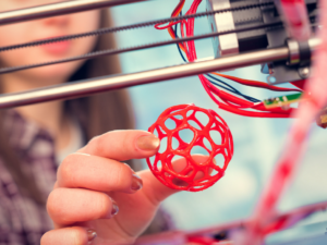 Opiskelija ottaa printtaamaansa palloa pois 3D-tulostimesta
