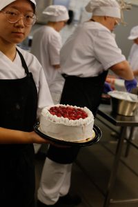 Opiskelija esittelee valmistamaansa mansikkakermakakkua