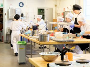 Opiskelijat opetuskeittiössä tekemässä sokerisia koristeita