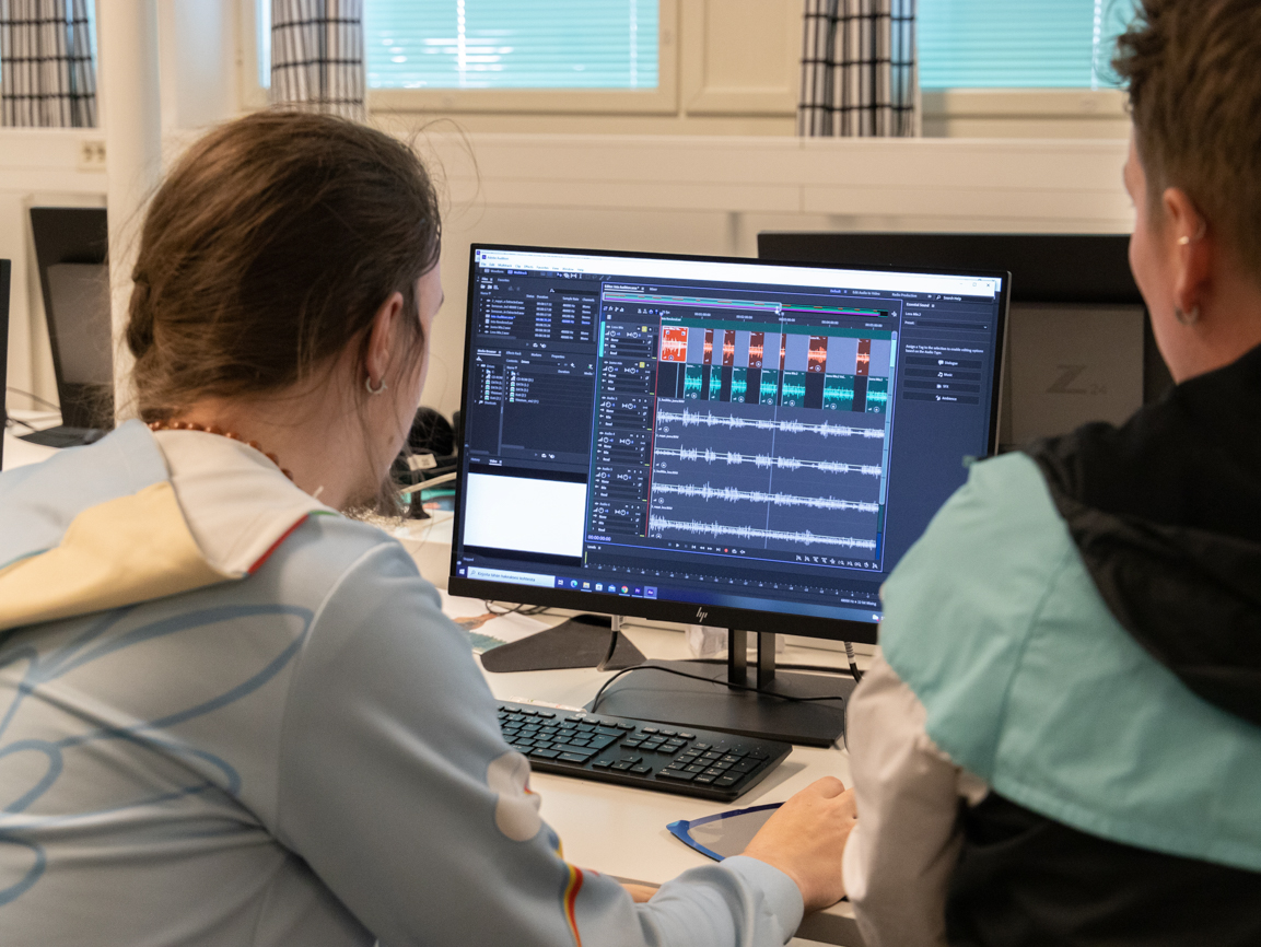 Opettaja opastaa opiskelijalle ääniraitojen editointia tietokoneella