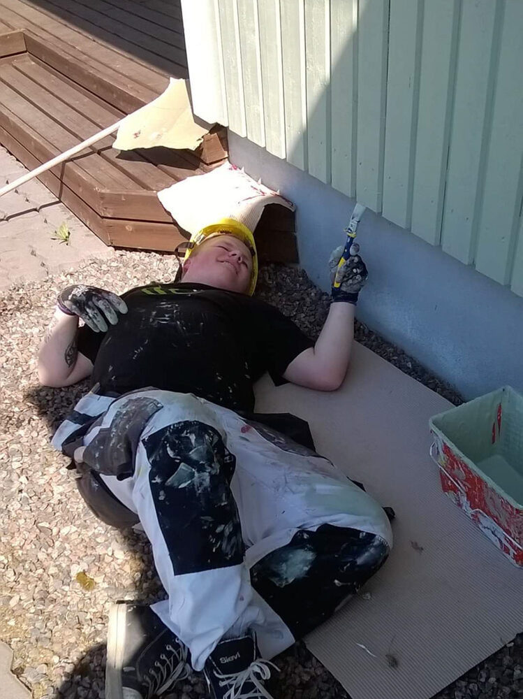 Pintapuolen opiskelija maalaa talon ulkovuorta hymyssä suin