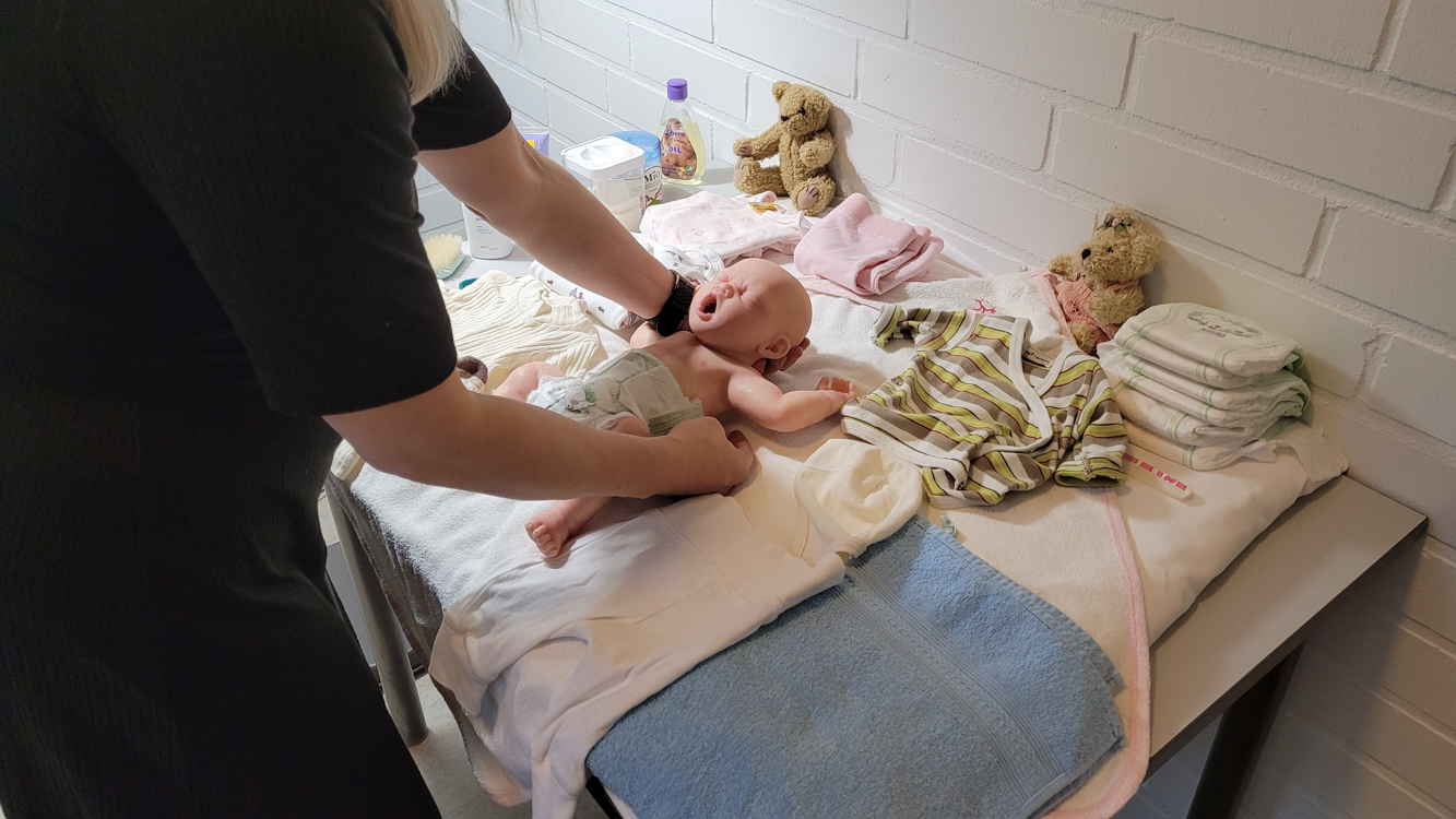 Opiskelija opettelee vaihtamaan vaippaa vauvanukelle