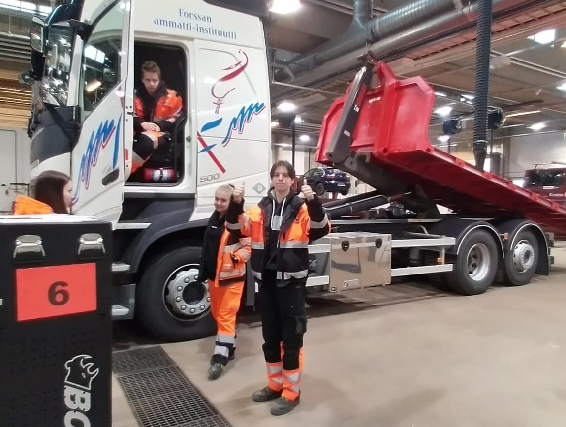 logistiikan opiskelija näyttää peukkuja kuorma-auton edessä muiden opiskelijoiden seistessä vieressä